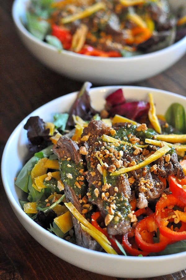 A bowl of Thai Steak Salad made with seasoned grilled Skirt Steak, a sweet cilantro sauce, and tossed with mango, peppers, honey peanuts, fresh mint, and your favorite mixed greens! 