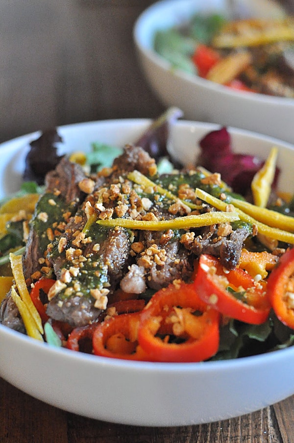 A bowl of Thai Steak Salad made with seasoned grilled Skirt Steak, a sweet cilantro sauce, and tossed with mango, peppers, honey peanuts, fresh mint, and your favorite mixed greens! 