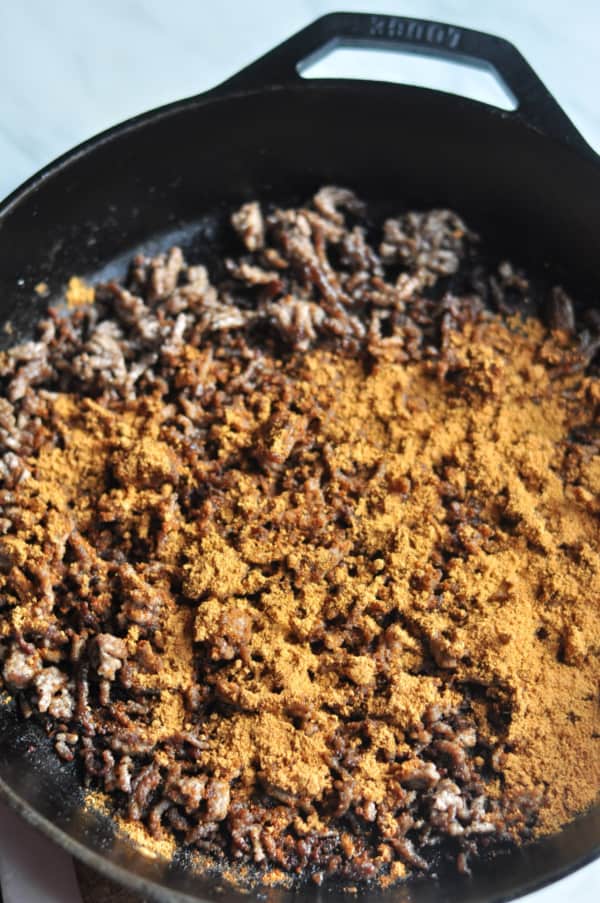 This easy Taco Salad is a quick recipe and is layered with Doritos, ground beef and your favorite taco toppings. Cast iron pan making browned meat and taco seasoning.