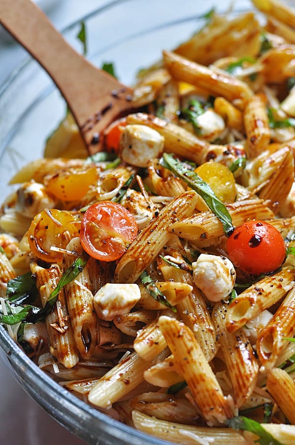 This Caprese pasta salad recipe is an easy make-ahead dish for weeknight dinner or potlucks. Made with basil, mozzarella, tomatoes, and balsamic glaze. Bowl of caprese pasta salad with fresh basil.